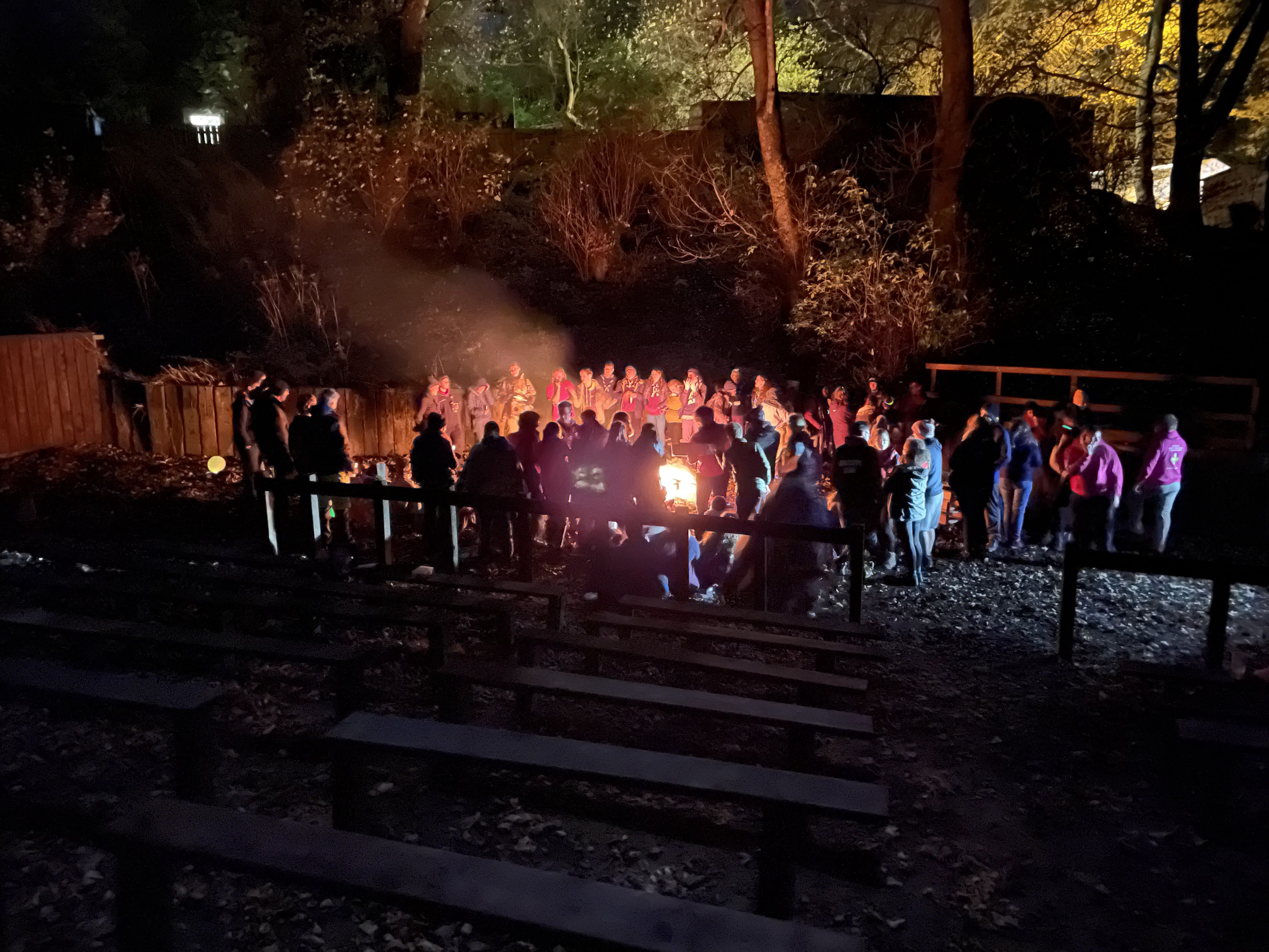 Wide shot from the back of the campfire arena, looking down to a large group huddled around the campfire